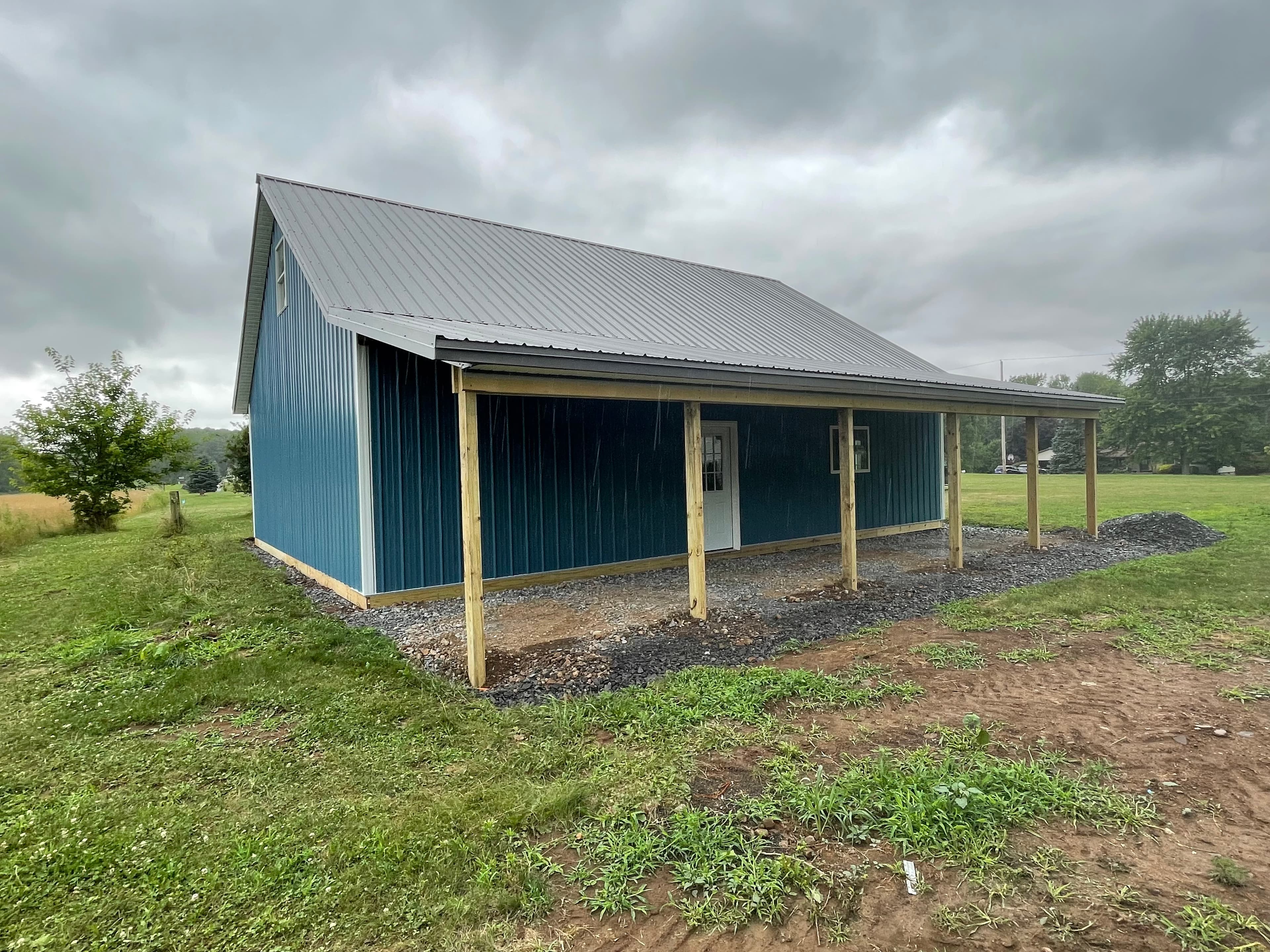 Blue metal pole barn with gray roof and covered porch on gravel base