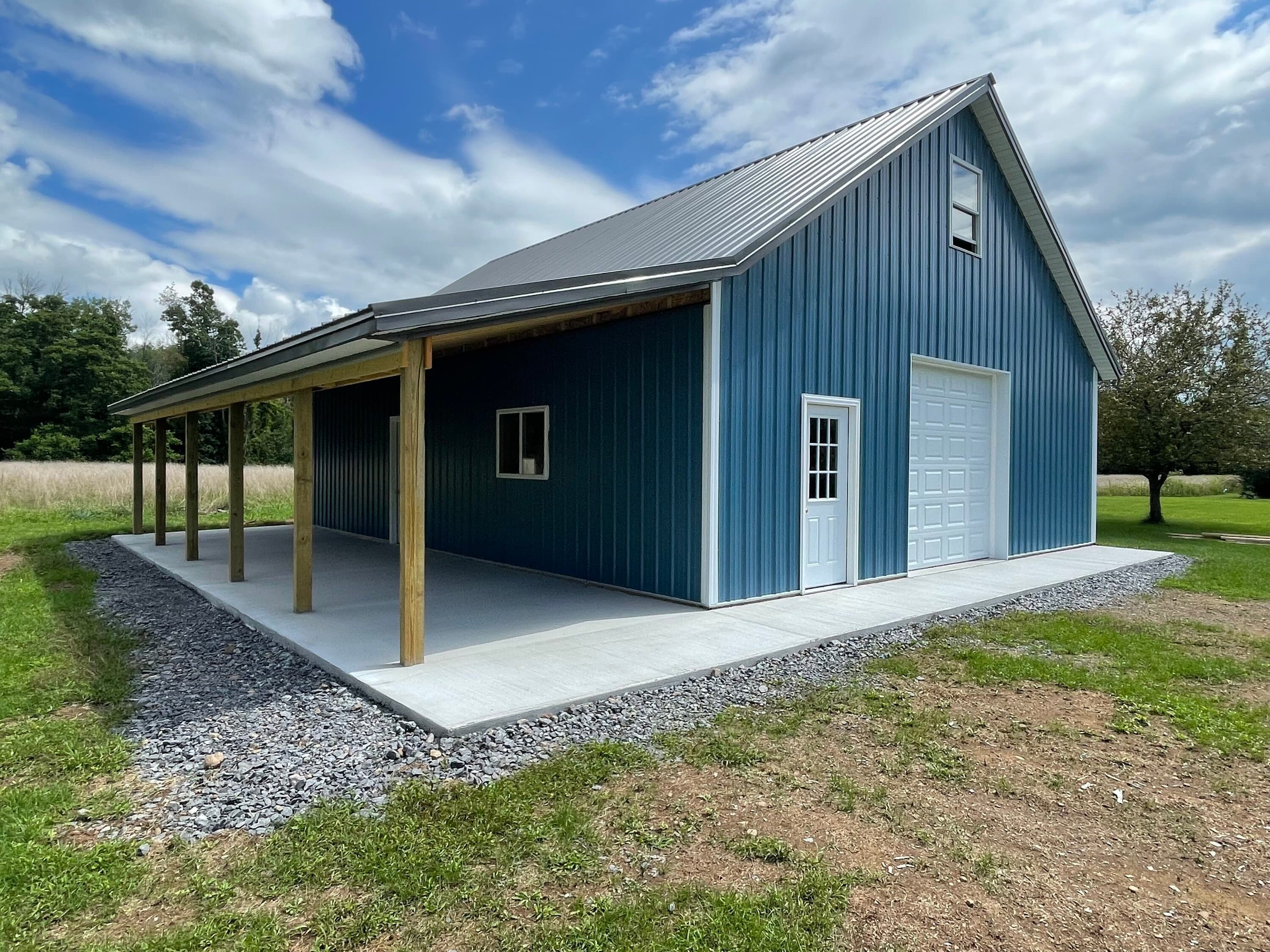 Blue metal pole barn with covered porch, garage door, and concrete pad