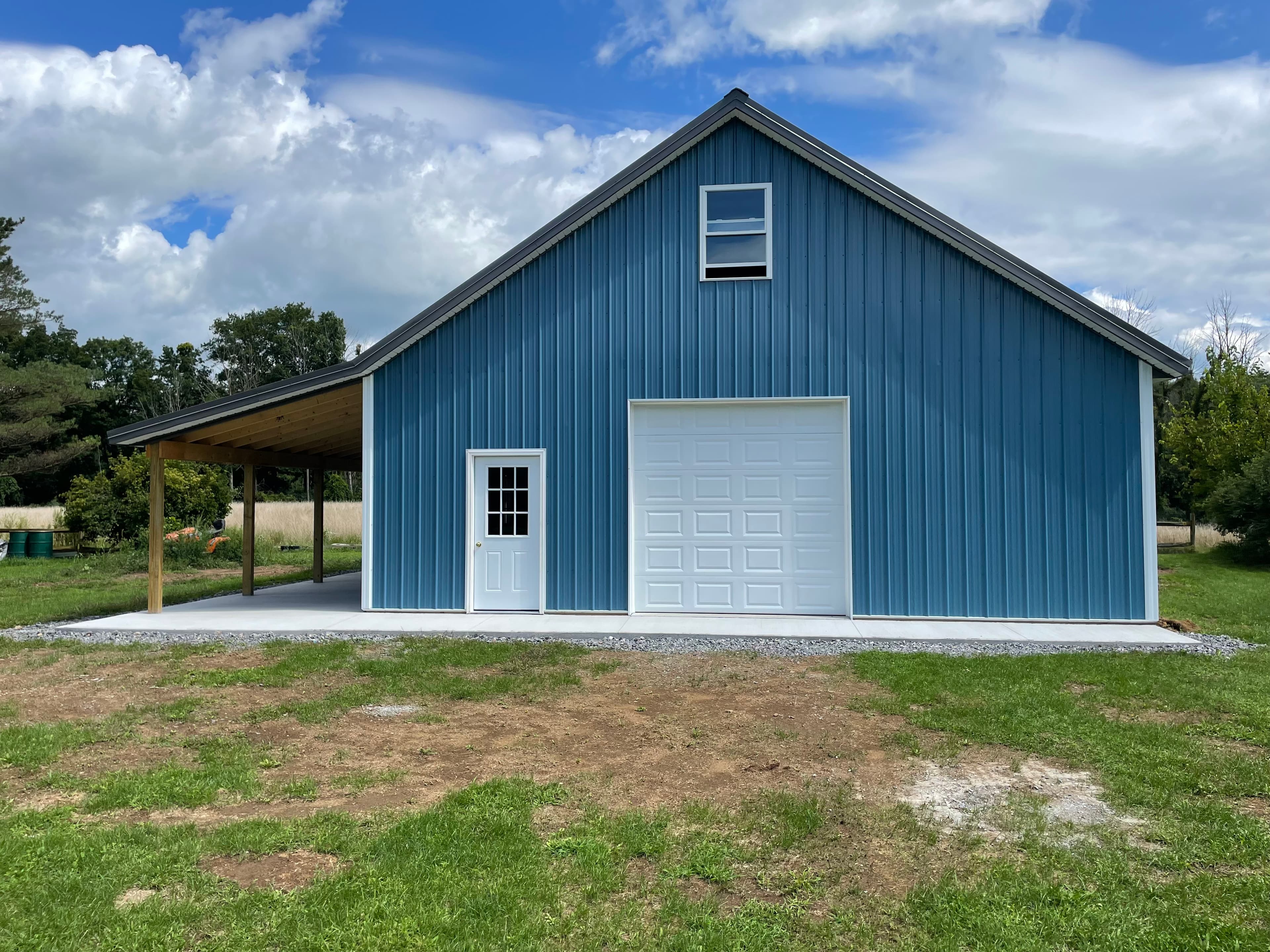 Blue metal pole barn with white garage door, entry door, and covered side porch