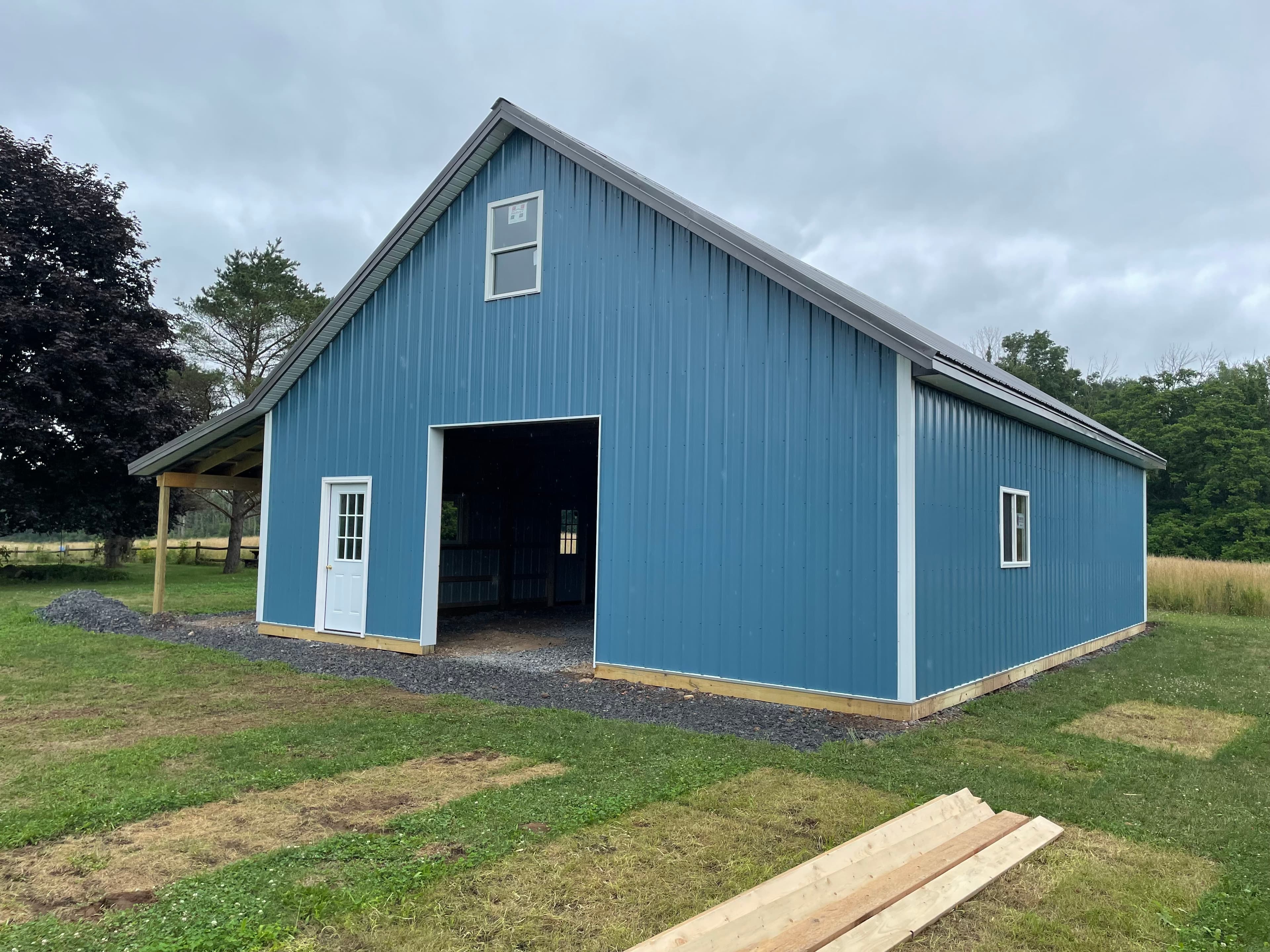 Blue metal pole barn with white trim and large center door opening