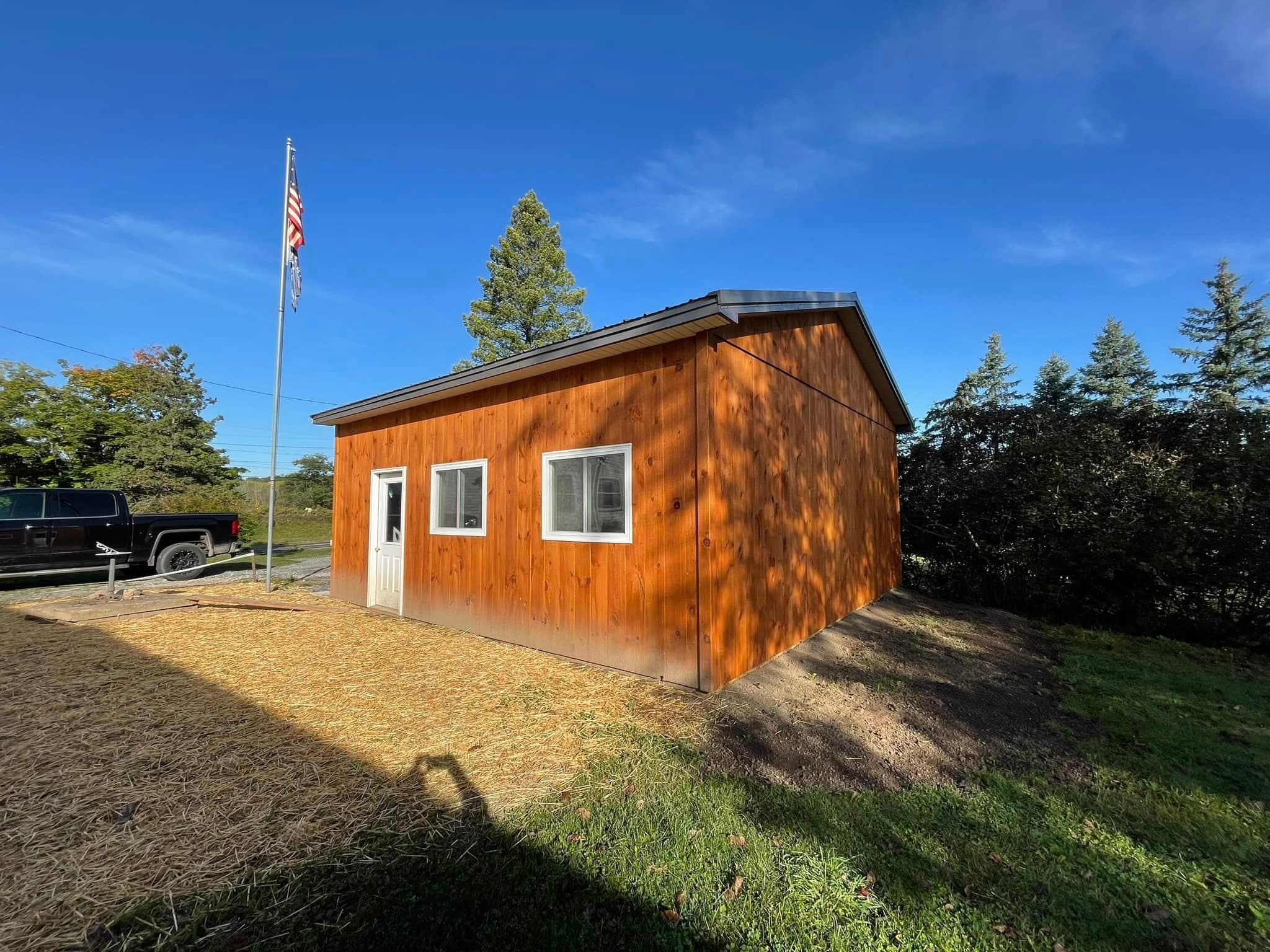 Cedar-sided storage shed with white trim windows and American flag pole