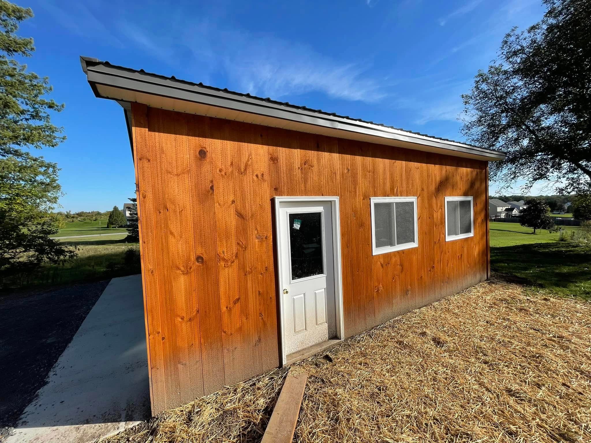 Small shed with natural wood siding, white door and windows, metal roof