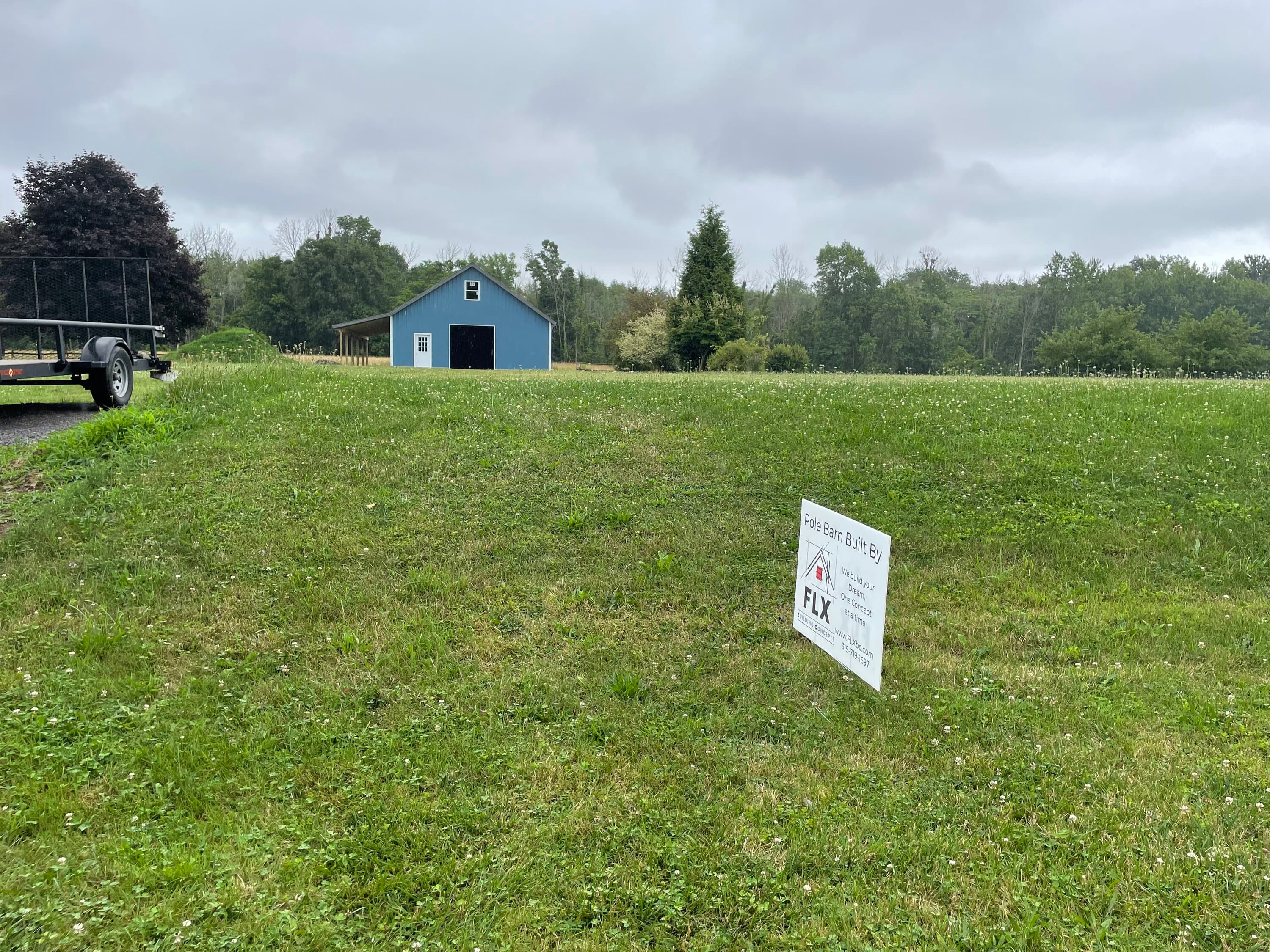 Blue pole barn and yard sign for FLX Building Concepts in grassy field