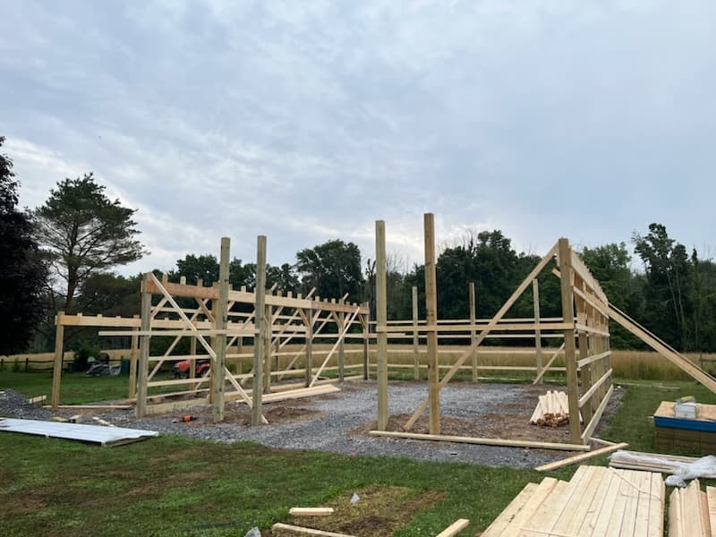 Timber frame structure of a pole barn under construction with vertical posts and diagonal bracing