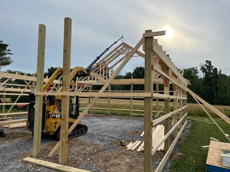 Timber frame pole barn under construction with CAT skid steer on gravel base