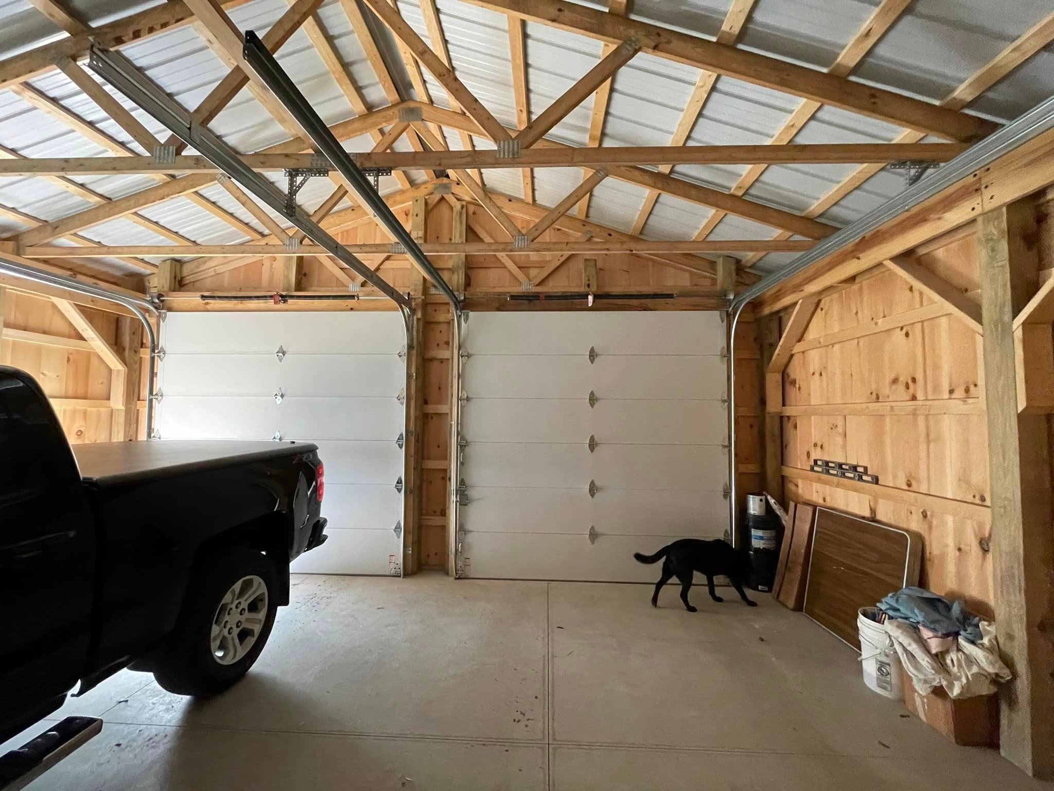 Interior of pole barn garage with exposed timber frame trusses and white overhead doors