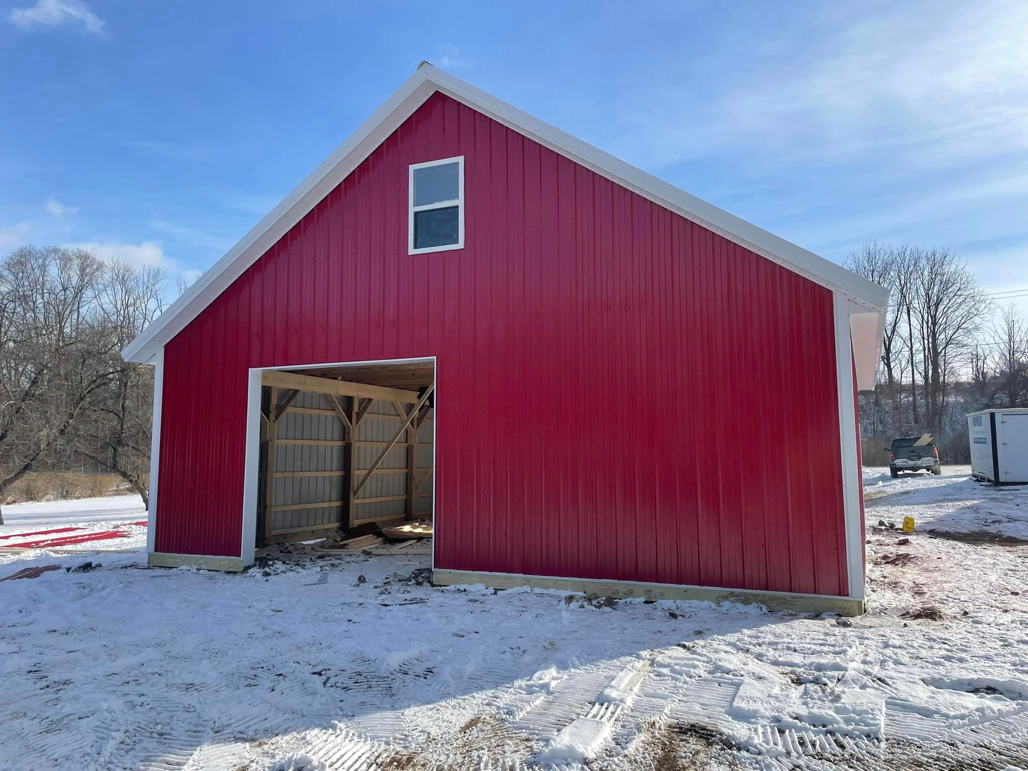 Red pole barn with white trim and open garage door in winter